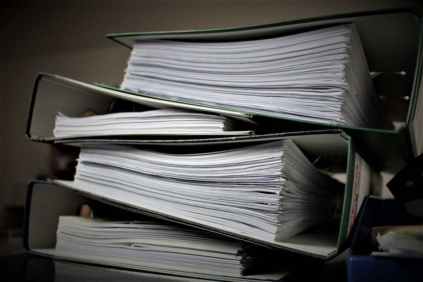 A stack of lever-arch binders packed with paper, left open on an office desk.