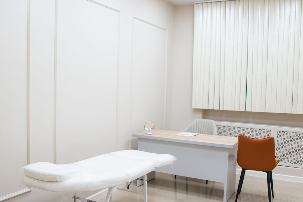 An empty medical exam room with the table made up and the desk clear.