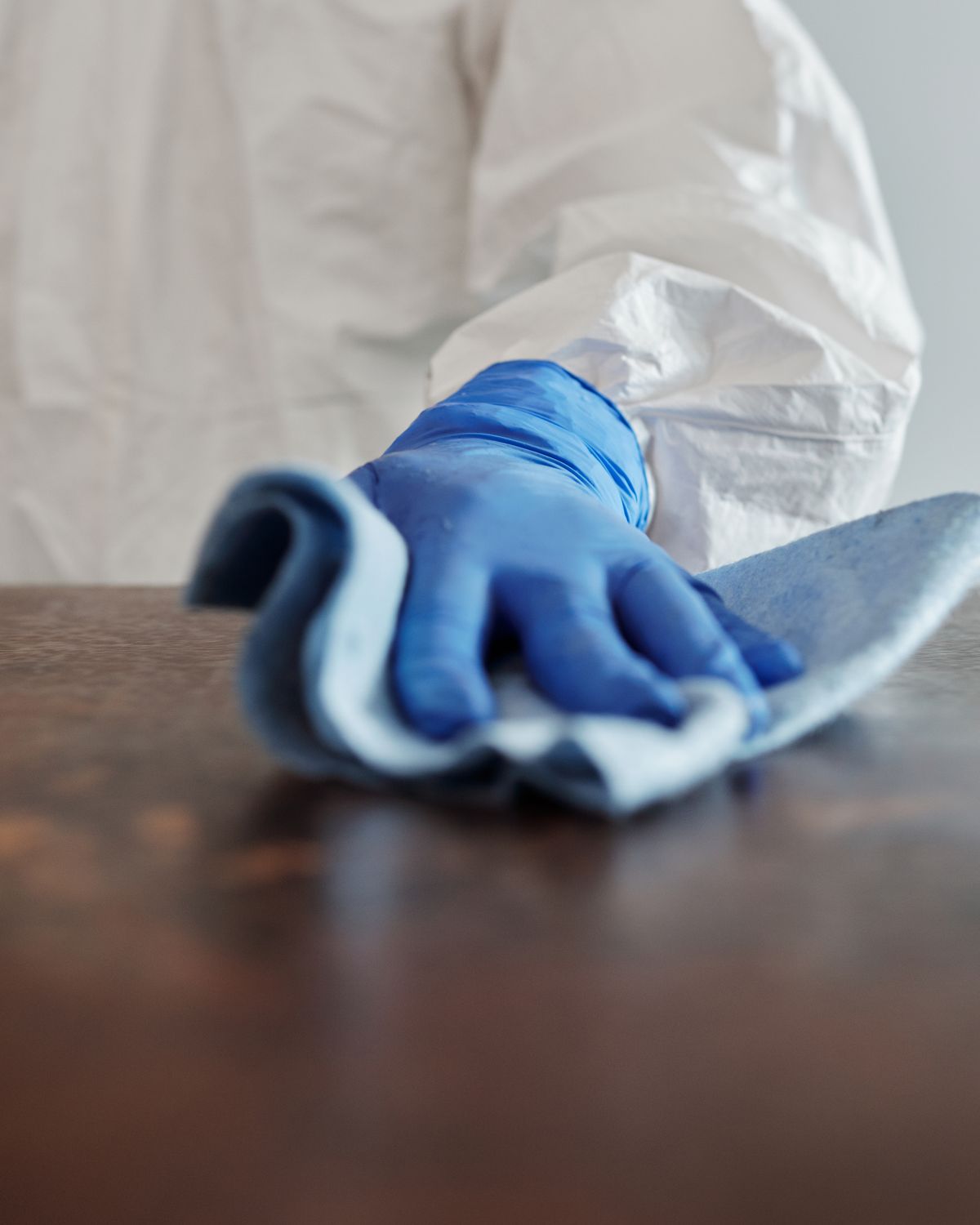 A gloved hand wiping a conference table with a microfiber cloth.