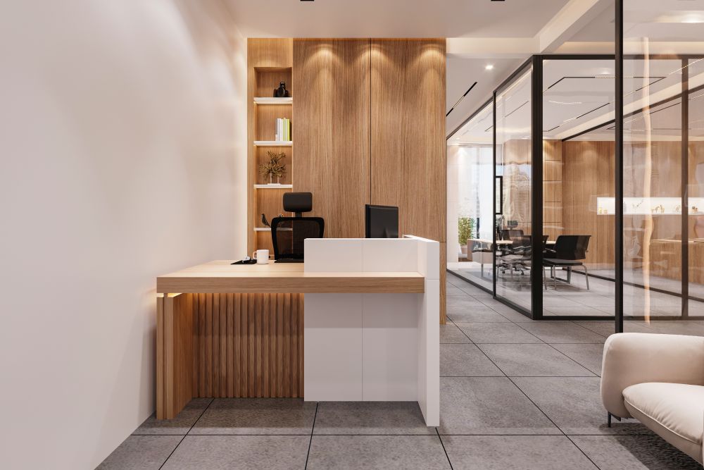 An office reception desk in wood and white, with a glass partition behind it.
